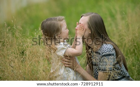  A little girl with blond hair in a beautiful dress closes her hands to her mother in the grass. Concept of happy friendly family.
