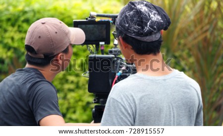 Blurry image of video production people making commercial movie with digital camera and equipment set at outdoor location.