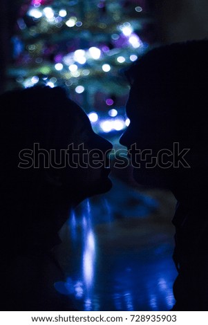 a couple in front of the Christmas tree in the gloom