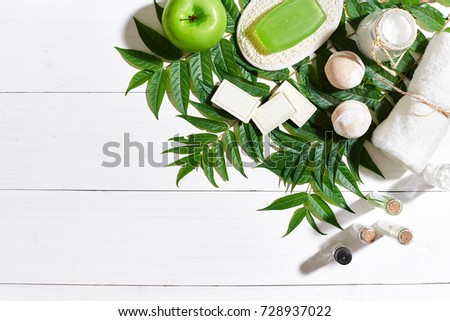 Spa set with towel and soap on white wooden background with green leaves