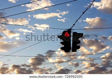 Silhouette of red traffic light against the blue sky with small clouds in sunset