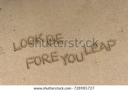 Handwriting  words "LOOK BE FORE YOU LEAP" on sand of beach.