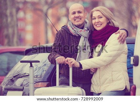 Joyful elderly spouses with luggage standing at street and smiling. Focus on man
