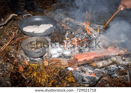 Fresh fish fillets frying on pan with boiled limpits and baked potatoes at camp fire Royalty-Free Stock Photo #729021718