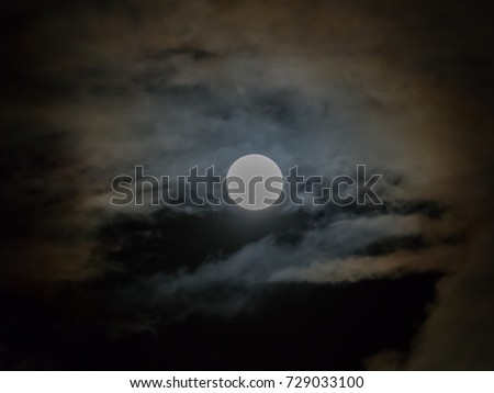 White full moon on dark clouds background. It is a black and white image that see details on the surface. Look again is awesome suitable for Halloween background. Moon orbit planet Earth.