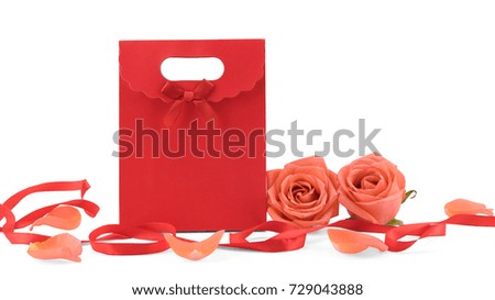 Red gift bag decorated with orange roses and petals and red ribbon isolated on white background