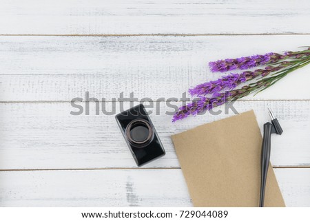 Blank brown card, oblique pen and bottle of ink decorated with violet liatris flowers on white wood background with copy space