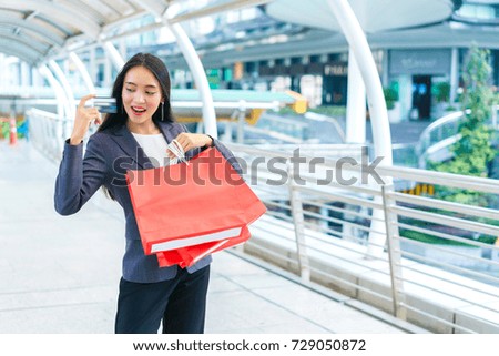 Happy asian business woman showing credit card and hold shopping bags at modern street. concept of purchasing, pre order, buyer, marketing and advertising.