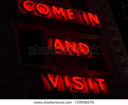 Neon sign on building that reads, "Come in and Visit"
