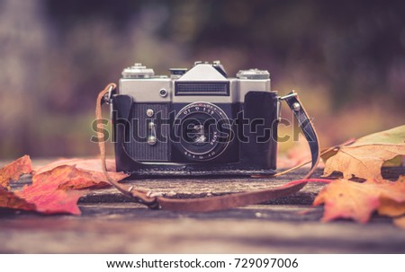 old camera on wooden background surrounded by autumn maple leaves