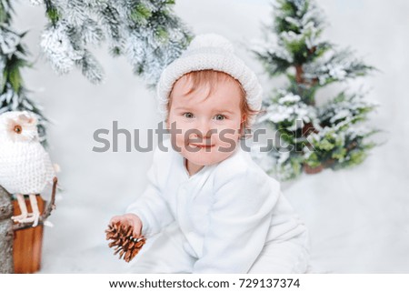 Little baby holding a cone sitting in the Christmas tree / Happy child with a bump in his hands in a New Year's decor