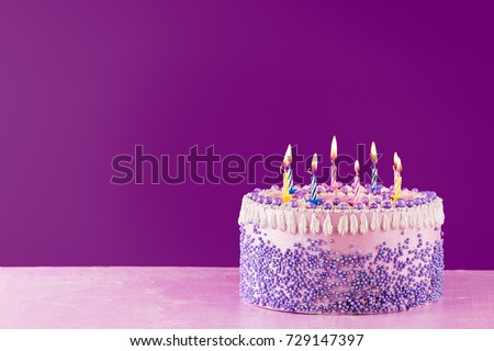 Pink Birthday cake with colorful candles over a bright purple background with copy space