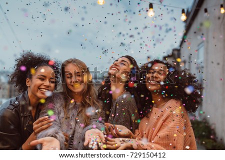 Four beautiful women standing at a terrace under confetti. Royalty-Free Stock Photo #729150412