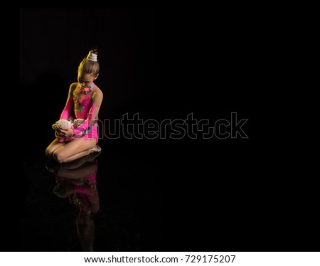 Young girl athlete gymnast with teddy bear in hands posing on black background