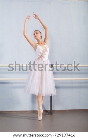 A ballerina in a white suit poses near the bars for ballet lessons