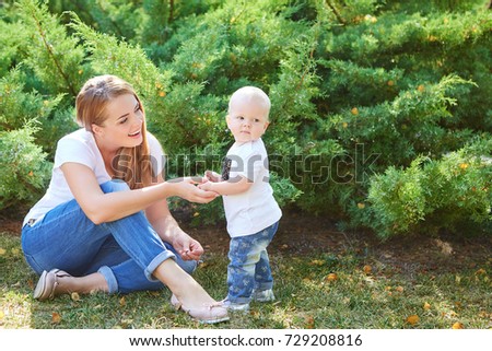 Happy beautiful mother and baby daughter or son enjoying in the summer park