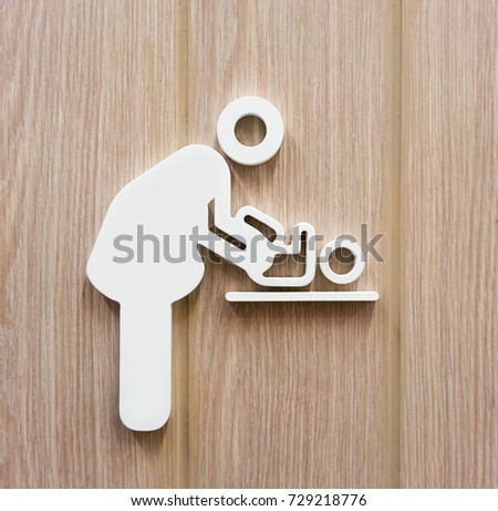 Woman and baby symbol changing diapers against wooden background.
