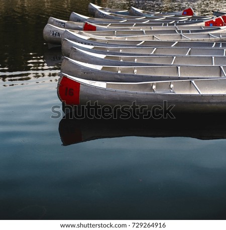 Grouping of multiple silver metal canoes on glassy blue lake