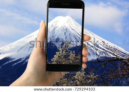 Hand of a hipster taking a photo of Mount Fuji view with smart phone. Teenage girl holding video camera for recording of Mount Fuji in Japan.