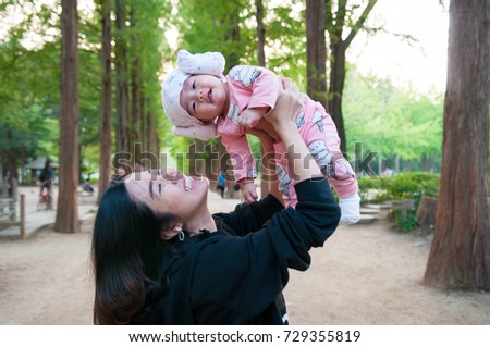Mother holding her newborn baby in pink clothes while her was smiling with happiness. Baby is smiling on her mother hand in public park. Single mom with her baby.