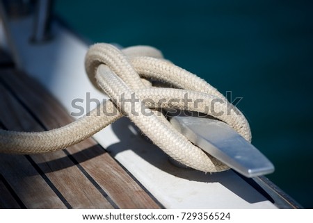 Closeup picture a rope tied to a metal cleat on a yacht deck.  