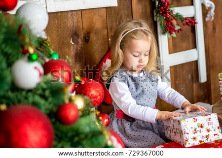 Beautiful happy girl unwrap christmas present box on holiday morning in beautiful room interior. Female child open Xmas gift near decorated fir tree. Winter holidays concept