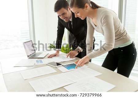 Smiling professional designers working on project at office desk, creating design for client concept, using color pantone swatches and construction plans of residential houses and commercial property