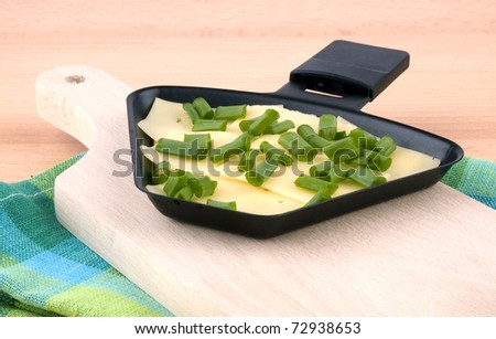 Closeup picture of raclette pan with cheese and spring onion on chopping board