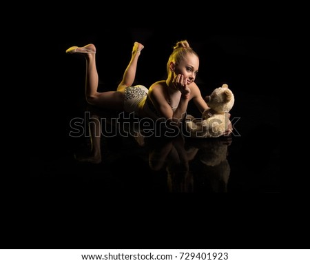 Young girl athlete gymnast with toy bear in hands posing on black background