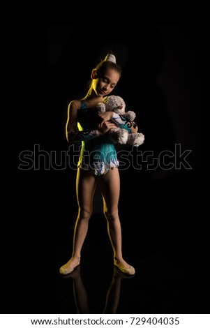 Young girl athlete gymnast with toy bear in hands posing on black background