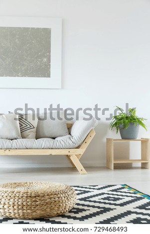Stylish pouf on geometric carpet in minimalist living room with grey sofa and silver painting