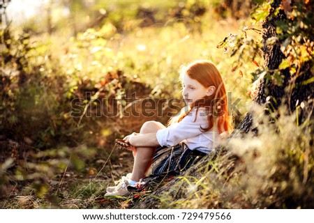 Autumn portrait of a red haired little girl sitting under a tree.