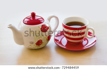 striped cup with tea on a saucer and brewer with a poppy picture on a wooden table top