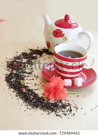 striped cup with tea on a saucer pieces of sugar cubes, semicircular spice, small wild strawberries and brewer with a poppy picture on a wooden table top, red flower