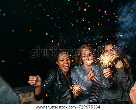 Group of happy friends celebrating new year's eve with confetti and sparklers Royalty-Free Stock Photo #729675334