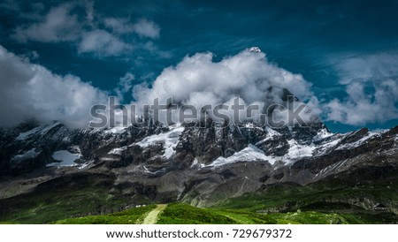 Landscape view of the south face of the Matterhorn, view from Plan Maison.Green meadow in the front, blue sky with white clouds above. Summer in the Pennine Alps, Valle d'Aosta, Italy, Europe.