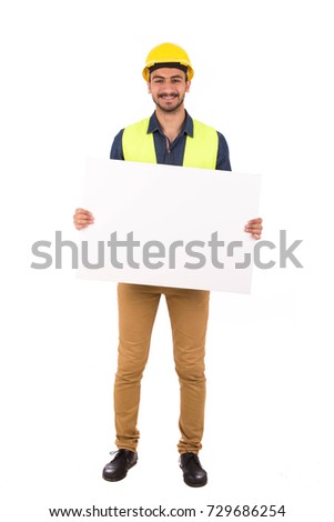 Handsome happy young engineer smiling and holding holding blank board, guy wearing blue shirt and beige pants with yellow vest, isolated on white background
