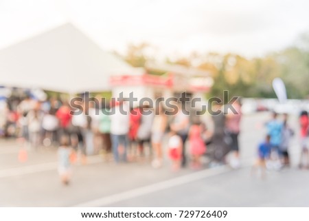 Blurred long people queuing for check-in at public event in Houston, Texas, US. Abstract background large group of diverse multiethnic visitors crowd family member, adult, kid waiting at tent entrance