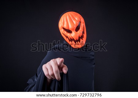 Mystery man with orange pumpkin evil mask pointing hand on black background, Halloween night costume concept