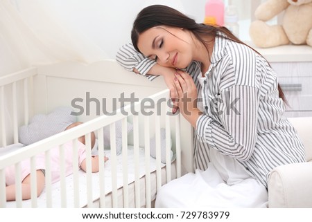 Mother near crib with sleeping baby at home