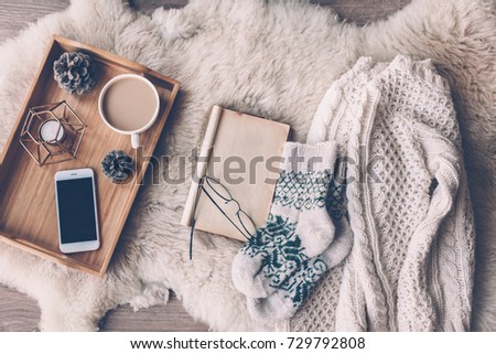 Mug with coffee, smart phone and home decor on wooden serving tray on sheep skin rug. Warm sweater, woolen socks and open book, winter weekend concept, top view  Royalty-Free Stock Photo #729792808