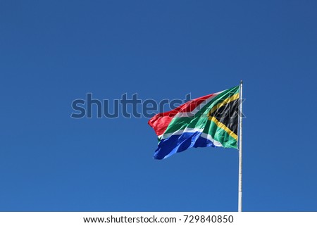 A South African flag on a flagpole with a blue sky background. 