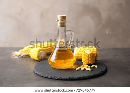 Glass pitcher with corn oil and cobs on grey background