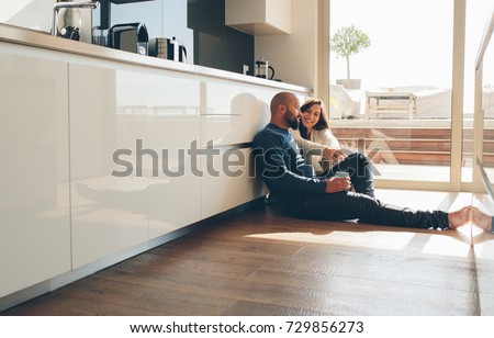 Young man and woman sitting on floor in kitchen and talking. Loving young couple spending time together at home. Royalty-Free Stock Photo #729856273