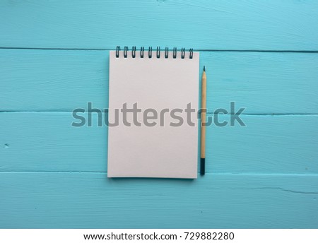 Notebook with a spring and a pencil. Bright blue, turquoise surface. Painted Board. Close-up with copy space. Top view