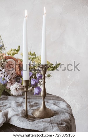 Analog film styled photo of beautiful wedding bouquet of roses in pastel shades with candles in vintage candlesticks in front view