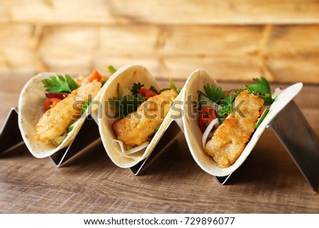 Stand with delicious fish tacos on wooden table