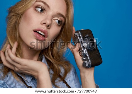 woman looking sideways in her hand a vintage camera on a blue background                               