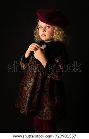 Vertical picture, isolated on black, cute caucasian blonde little girl in brown vintage dress, red tights and beret, hands on the chest, look at camera