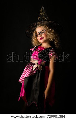 Vertical picture, isolated on black, cute caucasian blonde little girl in black dress with pink stripes, black scull hat and glasses, posing, look at camera